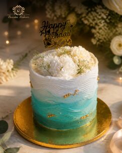 Blue and white ombre birthday cake with wave-textured frosting, white flowers, golden pearls, and elegant birthday topper.