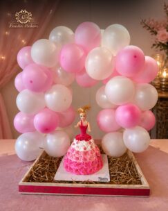 Princess doll birthday cake with pink buttercream design and decorative balloon arch arrangement.