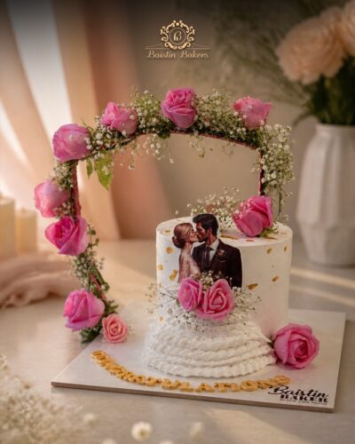 Romantic anniversary cake with floral arch, pink roses, and customized couple topper.