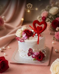 Elegant anniversary cake decorated with roses, butterflies, pearls, and heart topper.