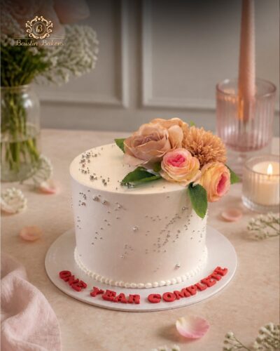 Elegant white floral celebration cake decorated with handcrafted flowers and silver pearls.